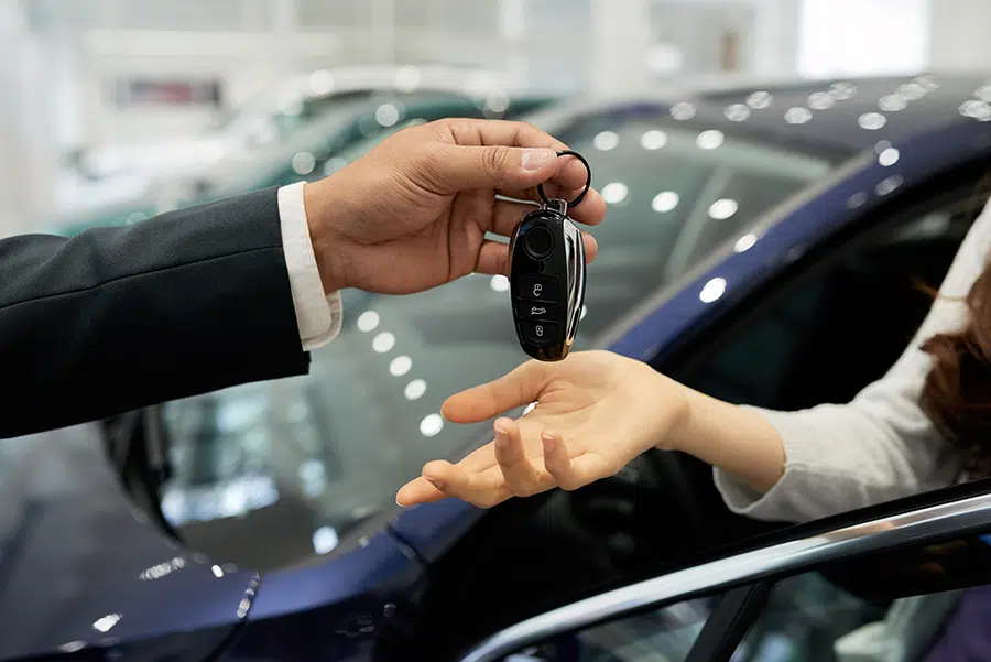 A man handing car keys to a woman with her hand out.