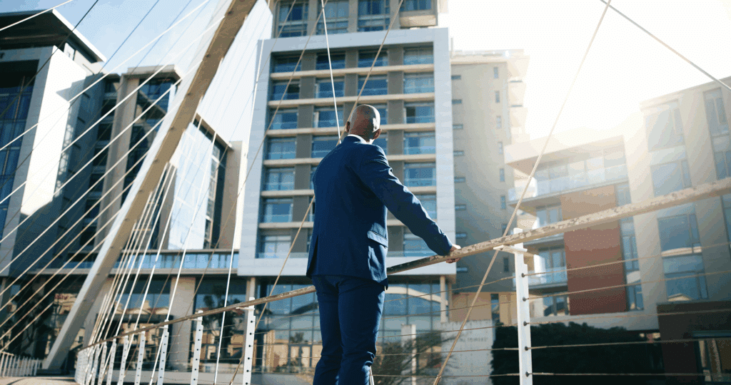 A man in a suit standing on a bridge overlooking an upscale apartment building.
