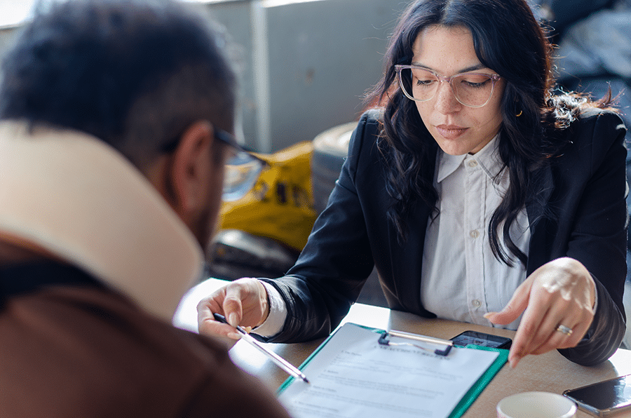 An attorney reviewing and pointing to a document across from her injured client wearing a neck brace.