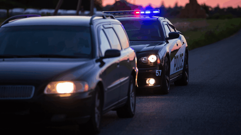 A police car with its lights on sitting behind a vehicle that was pulled over.