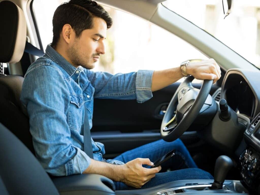 A man in a denim shirt texting while driving.