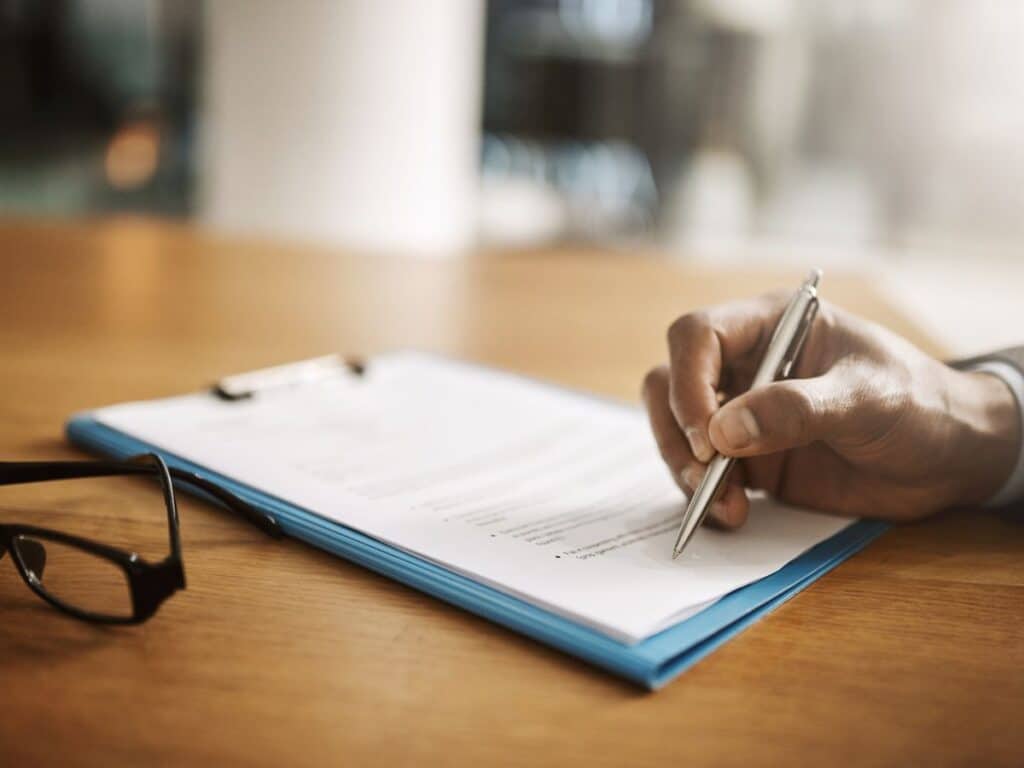 A man signing legal documents on a wooden desk.
