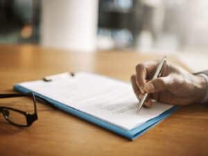 A man signing legal documents on a wooden desk.