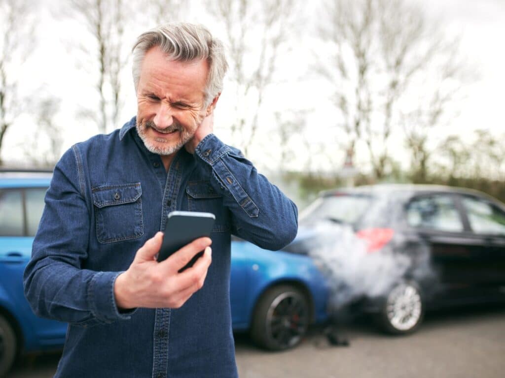 An older man holding his neck and grimacing after a two-car collision.