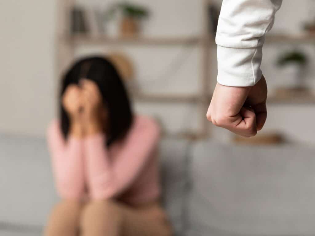 A man's closed fist with a woman hiding behind her hands in the background.