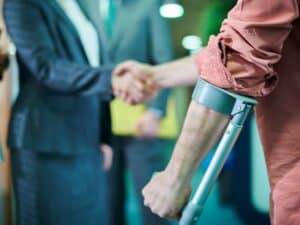 A man with crutches shaking hands with his personal injury attorney.