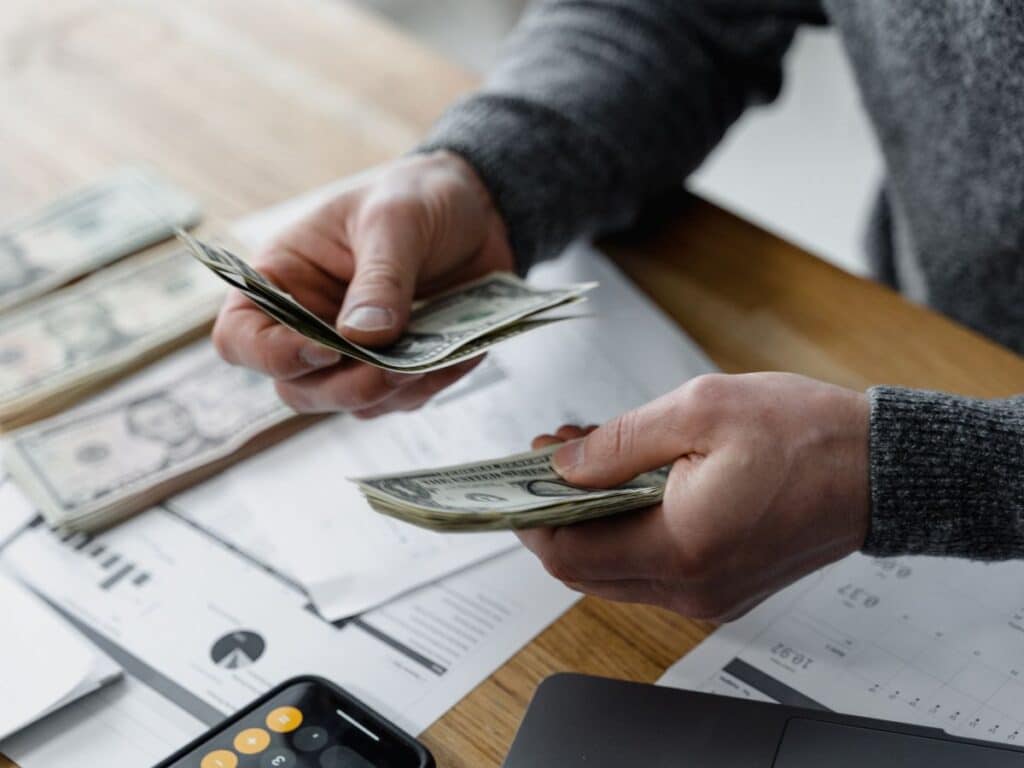 A man holding money with papers and a calculator on his desk.