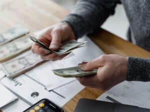 A man holding money with papers and a calculator on his desk.
