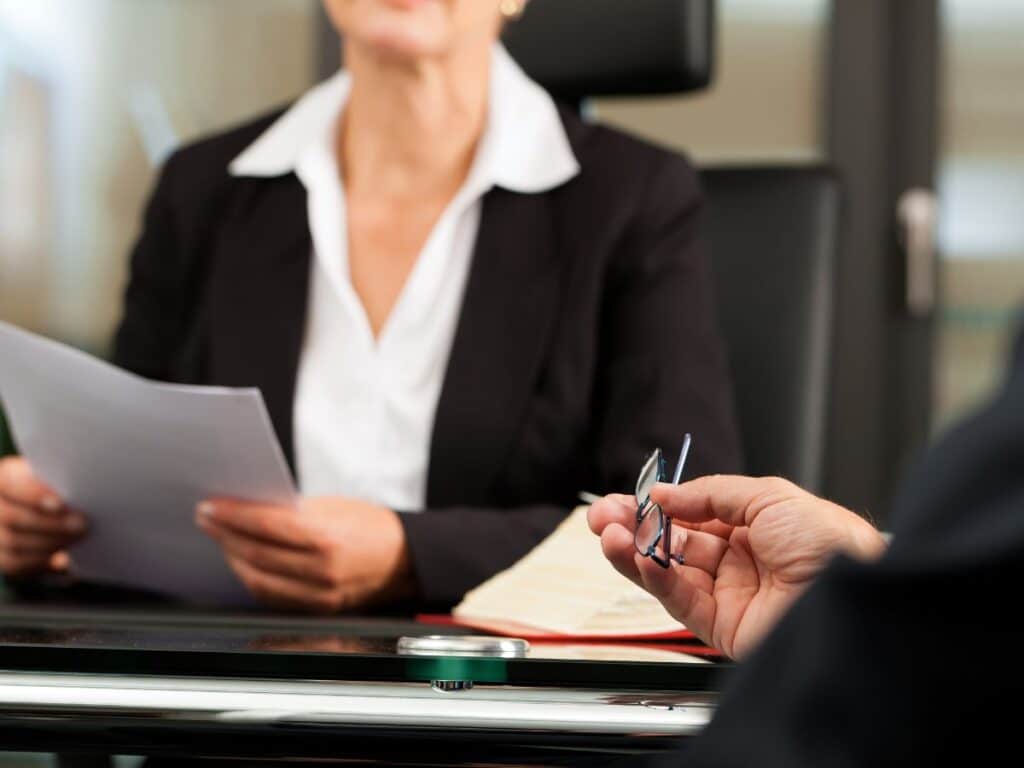 A man holding his glasses while conversing with his personal injury attorney in her office.