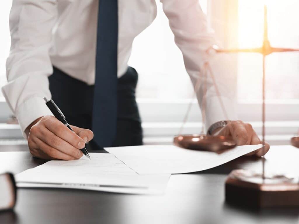A personal injury attorney standing over his desk while signing legal documents.