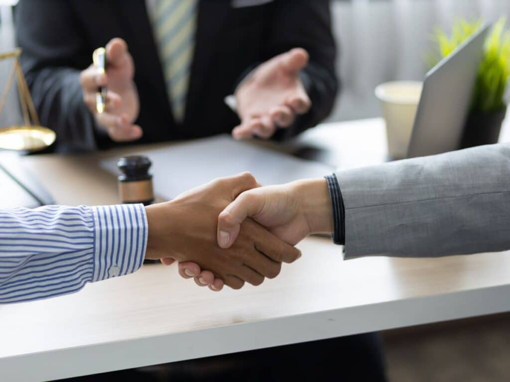 Two men shaking hands with their lawyer speaking in the background.