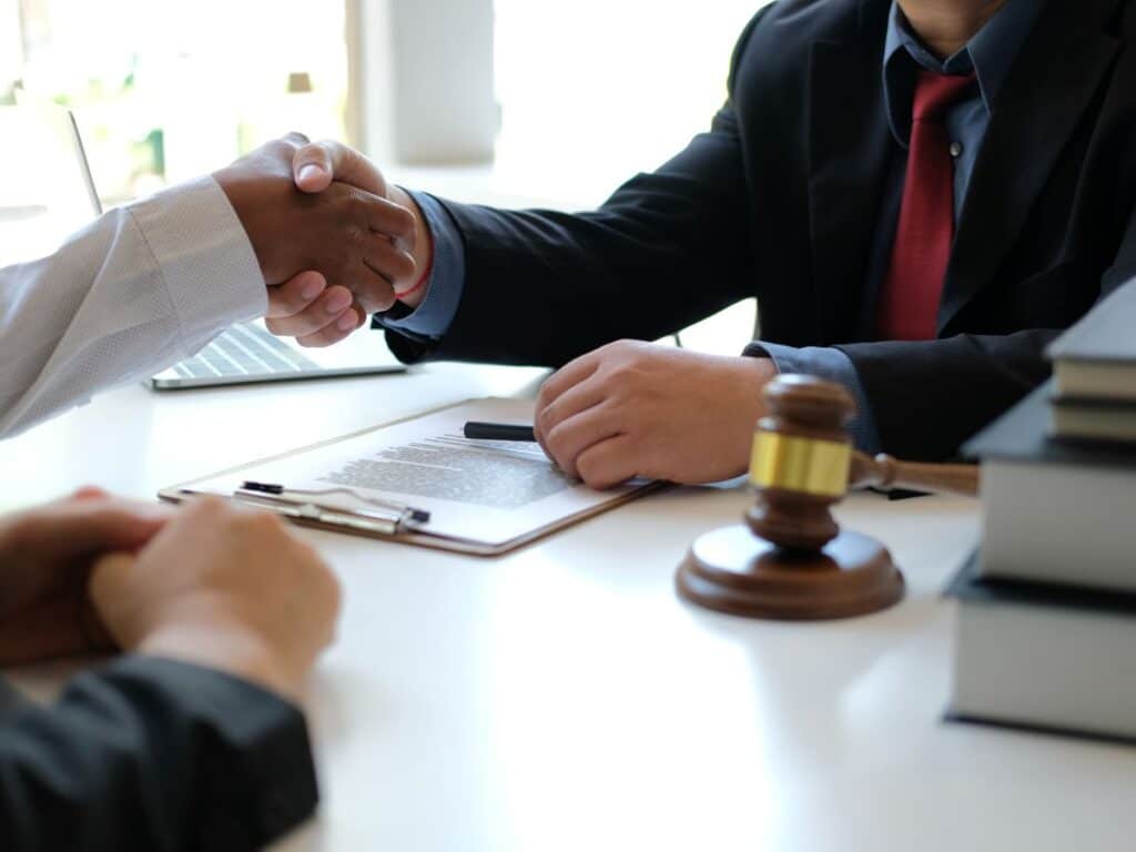 A personal injury lawyer shaking hands with one of his clients across his desk.