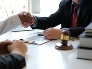 A personal injury lawyer shaking hands with one of his clients across his desk.