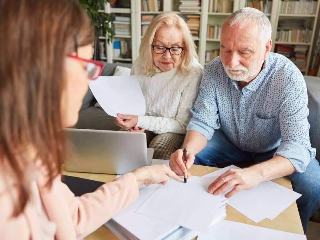 An elderly couple signing documents while sitting across from their personal injury lawyer.