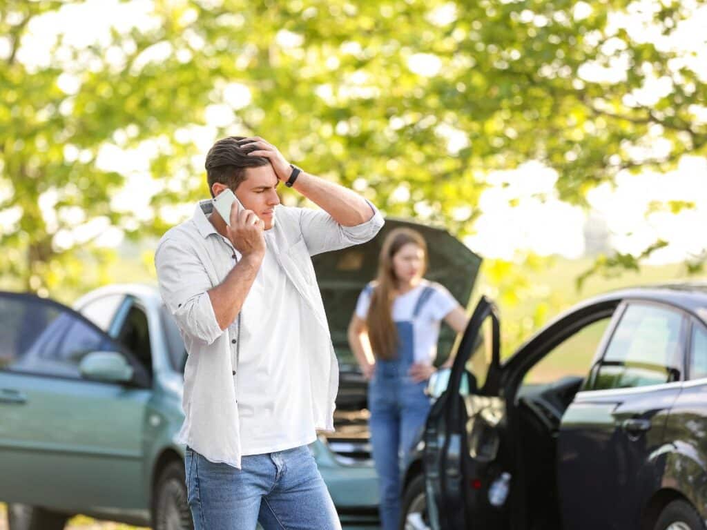 A man talking on the phone, and a woman checking out her car after a vehicle collision.