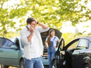 A man talking on the phone, and a woman checking out her car after a vehicle collision.