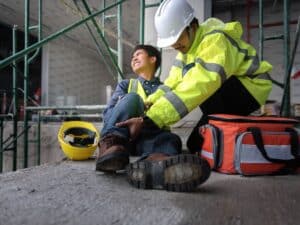 A construction worker in full gear tending to an injured coworker at a site.