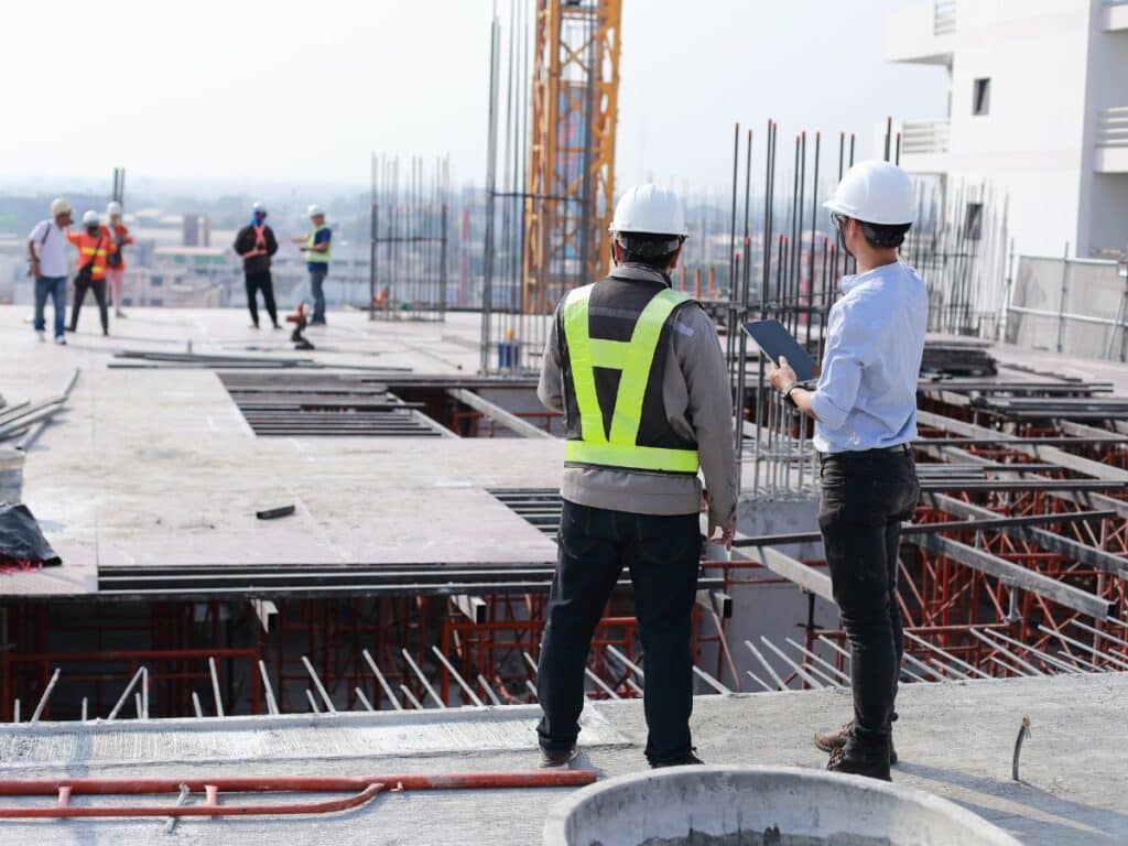 Two construction workers wearing hard hats looking out at a construction site.
