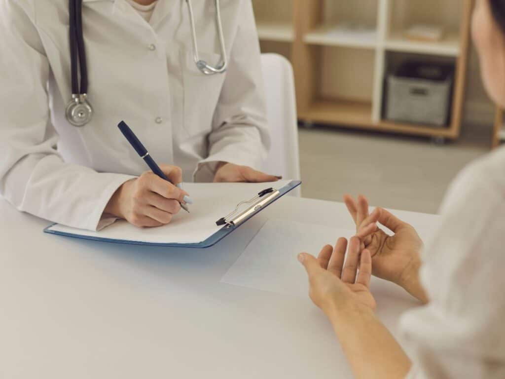 A woman talking to a doctor who is taking notes on a desk.