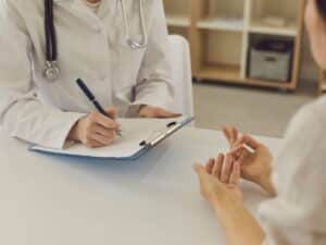 A woman talking to a doctor who is taking notes on a desk.