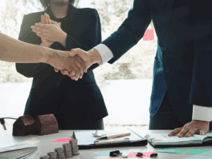 Two attorneys shaking hands over a desk while a woman watches on.