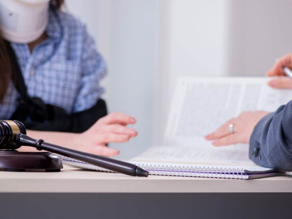 An injured woman with a neck brace and her arm in a sling sitting across from a personal injury attorney.